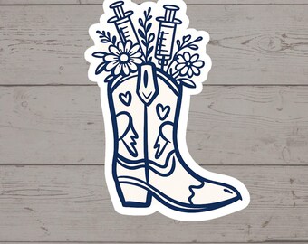 Puede incluir: Una pegatina troquelada que muestra una bota vaquera blanca con contornos azul oscuro. La bota está decorada con pequeños iconos de corazones y rayos. Del interior de la bota emergen dos jeringuillas médicas rodeadas de elementos florales.