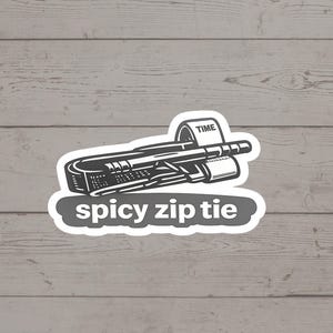 May include: A black and white sticker featuring a stylized zip tie with the word "TIME" on a label. The text "spicy zip tie" is below the zip tie in a gray oval.
