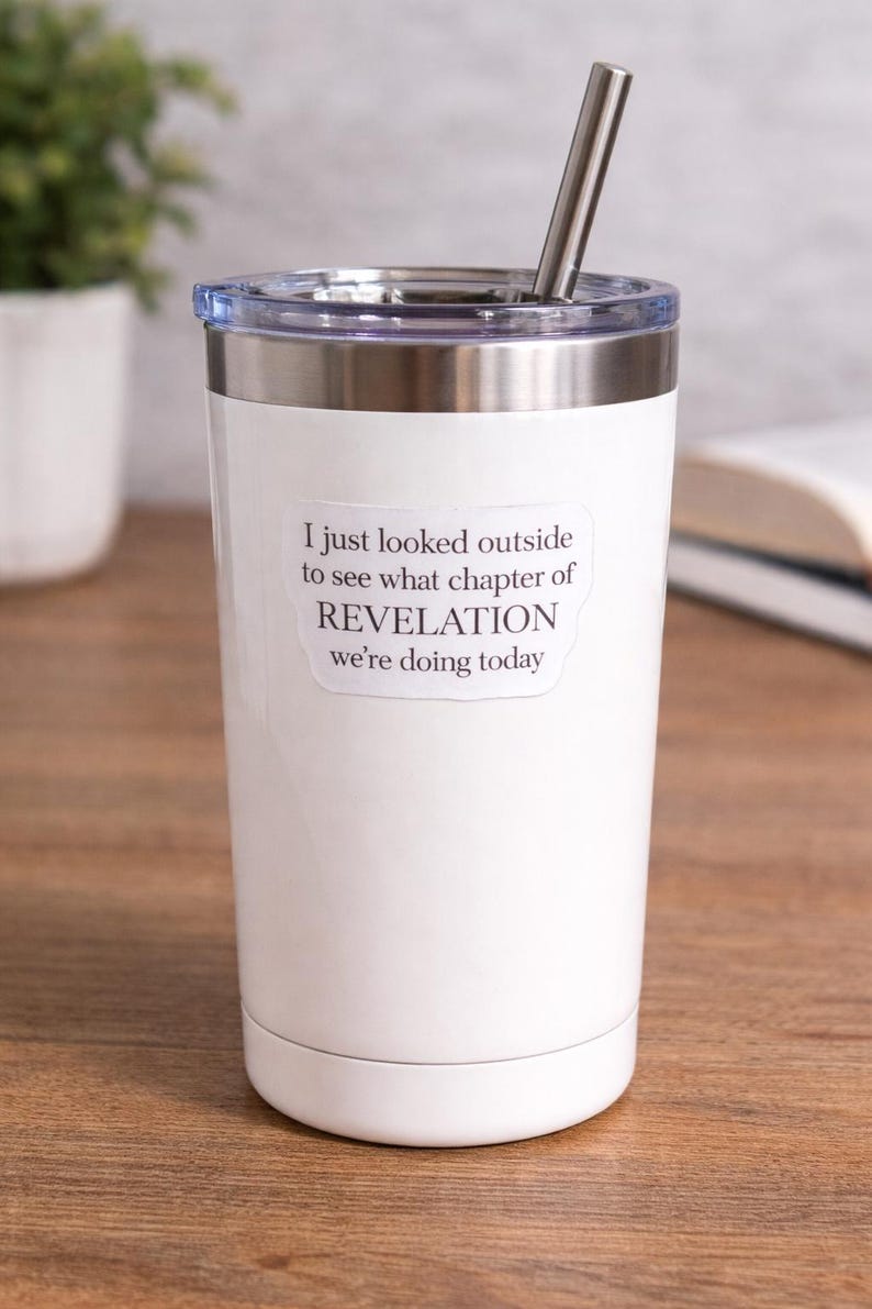 Op de afbeelding: Witte beker met een roestvrijstalen rand en een doorzichtig deksel. De beker heeft een roestvrijstalen rietje en een sticker met de tekst: "I just looked outside to see what chapter of REVELATION we're doing today."