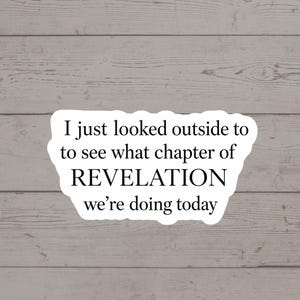 Op de afbeelding: Witte sticker met de tekst "I just looked outside to see what chapter of REVELATION we're doing today" in zwarte letters. De sticker staat op een lichtgrijze houten achtergrond.