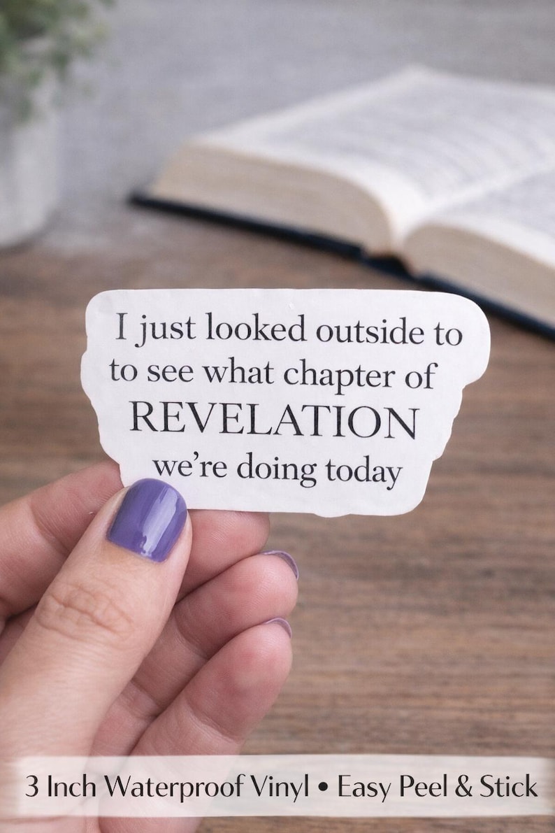 Op de afbeelding: Witte sticker met de tekst "I just looked outside to see what chapter of REVELATION we're doing today." De sticker wordt vastgehouden door een hand met paarse nagellak. Op de achtergrond is een boek te zien.