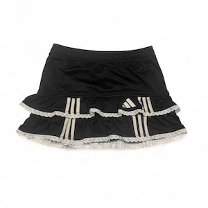 May include: Black athletic skirt with two ruffled layers and white lace trim. Features the Adidas logo and three white stripes on each side. The skirt is designed for sports and casual wear.