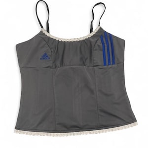 May include: Gray camisole with black spaghetti straps, featuring the Adidas logo in blue on the chest. Three blue stripes are on the right side. The top is trimmed with white lace.