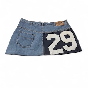 Peut inclure: Mini-jupe en jean avec un patch en cuir Route 66. La jupe présente un tissu en jean bleu clair d'un côté et un panneau bleu marine avec le numéro "29" en blanc de l'autre. Elle a une conception classique à cinq poches.