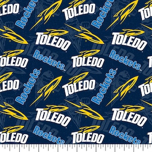 May include: A navy blue fabric with a repeating pattern of the words "Toledo Rockets" in white and yellow. The pattern also includes a stylized rocket ship graphic.