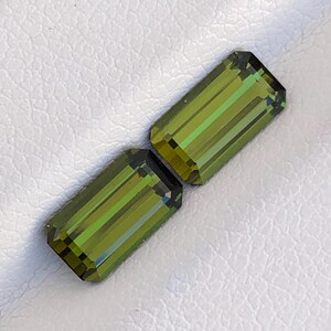 May include: Two emerald green rectangular gemstones with a faceted cut.