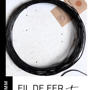 May include: A coil of black wire, 1.5 mm thick, is displayed against a white background. The text "FIL DE FER recuit" is at the bottom. A small brown tag with text and a logo is visible.