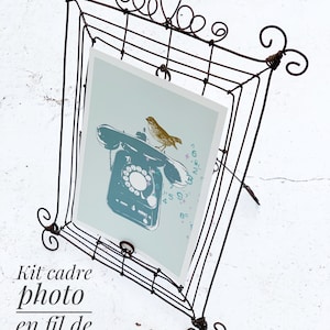 Puede incluir: Un marco de fotos de alambre marrón oscuro, de forma cuadrada, con una impresión de un teléfono vintage y un pájaro. El marco tiene espirales decorativas en la parte superior y en las esquinas. El texto "Kit cadre photo en fil de fer" está impreso en la parte inferior izquierda.