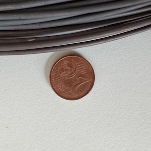 May include: A copper one-cent coin next to a coil of grey cable. The coin is on a white surface. The coin has a design of a globe and the number 1. The cable is dark grey and appears to be electrical wire.