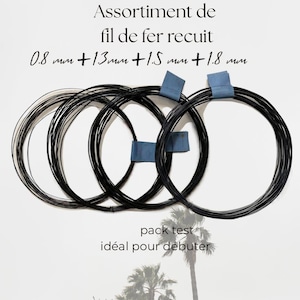 Puede incluir: Cuatro bobinas circulares de alambre de hierro recocido negro con cierres de cinta azul. El texto dice Assortment de fil de fer recuit 0.8 mm + 1.3 mm + 1.5 mm + 1.8 mm y pack test idéal pour débuter. Los diámetros del alambre están en milímetros.
