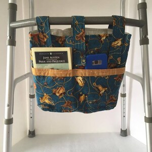 K&ouml;nnte beinhalten: Eine blaue und braune Stofftasche mit Western-Design h&auml;ngt an einem Rollator. Die Tasche hat mehrere F&auml;cher und enth&auml;lt ein Buch mit dem Titel "Stolz und Vorurteil" von Jane Austen und ein blaues Telefon.
