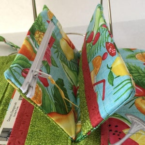 Pode incluir: Uma carteira de tecido turquesa com um bolso com z&iacute;per e uma estampa de frutas tropicais. A carteira est&aacute; aberta para mostrar o interior. O tecido &eacute; de algod&atilde;o e tem uma textura macia e acolchoada.