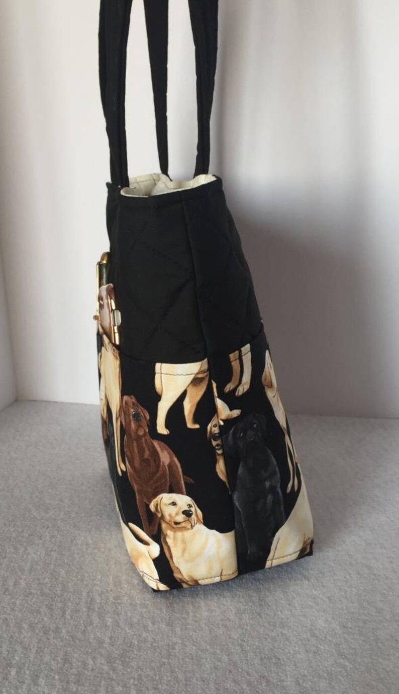 May include: Black quilted tote bag with a zippered pocket and a print of Labrador Retrievers in various colors. The bag has two black straps.