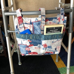 May include: A walker with a fabric bag hanging from the handles. The bag is decorated with a Parisian theme and has a book titled "Pride and Prejudice" by Jane Austen inside.