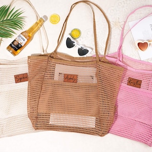 以下が含まれることがあります： ベージュ、ブラウン、ピンクのメッシュトートバッグ3つ。それぞれにパーソナライズ用の革製パッチが付いています。バッグには長いハンドルとフロントポケットがあります。サングラス、ビール瓶、レモンスライスなどのアクセサリーがあります。