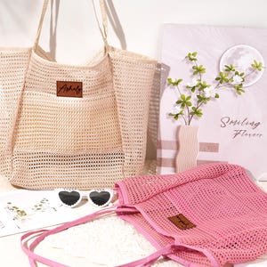 Pu&ograve; includere: Una borsa tote in rete beige e una borsa tote in rete rosa con etichette in pelle. Sono presenti anche una bottiglia di birra Corona, occhiali da sole a forma di cuore e una stampa floreale decorativa. La stampa floreale recita "Smiling Flowers".