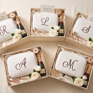 May include: Five gift boxes containing white quilted pouches with embroidered letters R, L, S, A, and M. Each box includes a small bottle of Moet champagne, a perfume bottle, lip products, white roses, and a card reading Thank You, Bridesmaid.