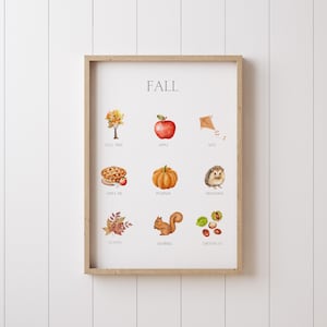 Puede incluir: Un estampado enmarcado en acuarela con un marco de madera clara. El estampado presenta la palabra "FALL" en la parte superior, con ilustraciones de elementos temáticos de otoño como un árbol, una manzana, una cometa, tarta de manzana, calabaza, erizo, hojas, ardilla y castañas.