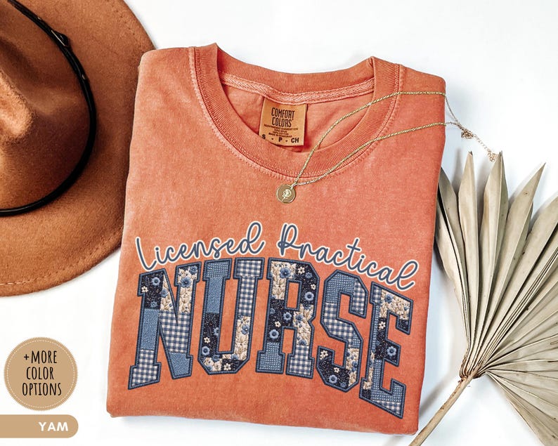 May include: A coral-colored t-shirt with the words "Licensed Practical NURSE" in a collegiate style. The letters are a mix of blue floral and plaid patterns. A gold necklace and a brown hat are also in the image.