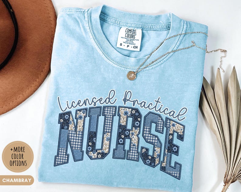 May include: Light blue t-shirt with the words "Licensed Practical Nurse" in a decorative font. The word "NURSE" is in a patchwork design with floral and gingham patterns. A gold necklace and a brown hat are also in the image.