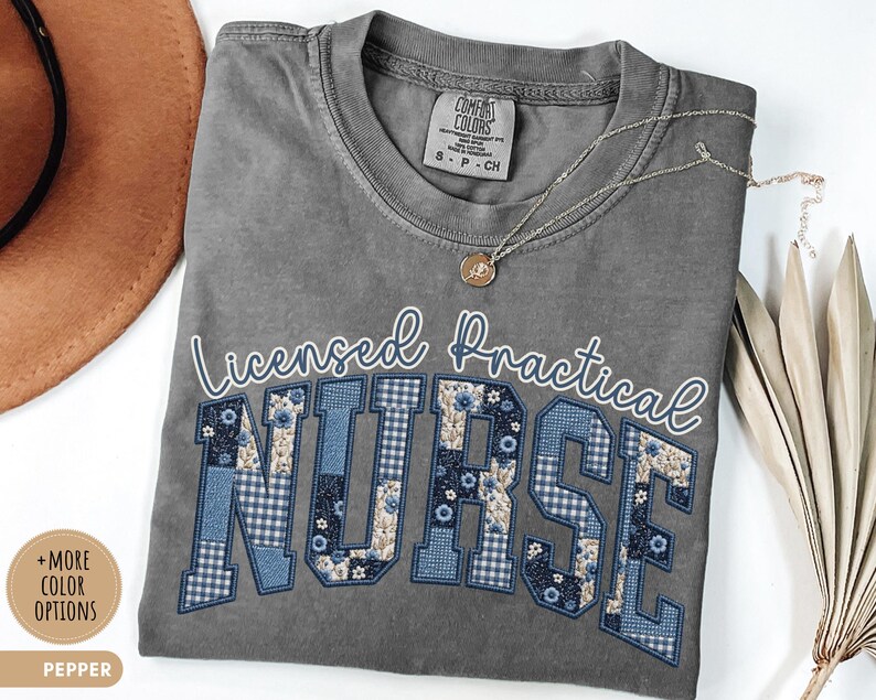 May include: A gray Comfort Colors t-shirt with the words "Licensed Practical Nurse" in white script and blue patchwork letters. A gold necklace with a pendant rests on the shirt. The shirt is size S-P-CH.