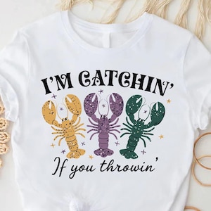 May include: White t-shirt with a graphic of three lobsters and the text "I'm Catchin' If you throwin'"