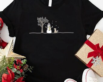 May include: Black t-shirt with a white snowman and a dog in the snow. The snowman is wearing a black hat and a scarf. The dog is wearing a scarf.