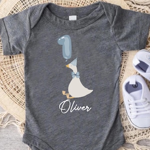Puede incluir: Un body de beb&eacute; gris con un pato blanco sosteniendo un globo azul. El body tiene el nombre "Oliver" impreso.