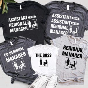 May include: Set of five t-shirts with a white graphic of a person sitting at a desk with a computer. The shirts have the text "Assistant to the Regional Manager", "Assistant to the Assistant Regional Manager", "Co-Regional Manager", "The Boss", and "Regional Manager".