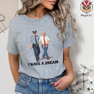 May include: A gray t-shirt featuring a graphic of a police officer and a man in a white shirt and red tie. The text "I HAVE A DREAM" is printed below the graphic. The shirt has short sleeves.