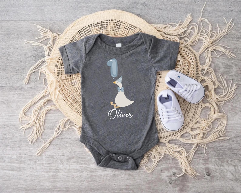 Puede incluir: Un body de beb&eacute; gris con un pato blanco sosteniendo un globo azul. El body tiene el nombre "Oliver" impreso.