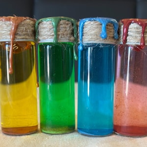 May include: Four small glass bottles with cork stoppers and twine wrapped around the necks. The bottles contain different colored liquids: yellow, green, blue, and pink.