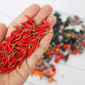 May include: A hand holding a pile of small, bright red chili peppers. The peppers have green stems and are arranged in a loose pile.