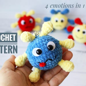 May include: Crochet pattern for a blue, yellow, and red plush toy with a face and four different expressions. The text "4 emotions in 1 toy" is visible above the toy. The text "CROCHET PATTERN" is visible below the toy.