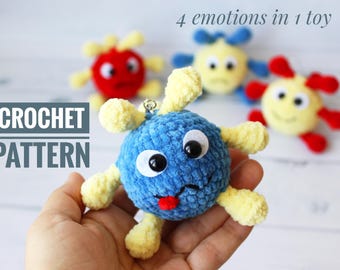 May include: Crochet pattern for a blue, yellow, and red plush toy with a face and four different expressions. The text "4 emotions in 1 toy" is visible above the toy. The text "CROCHET PATTERN" is visible below the toy.