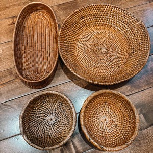 May include: Four woven wicker baskets in different sizes and shapes. The baskets are brown and have a natural, rustic look.