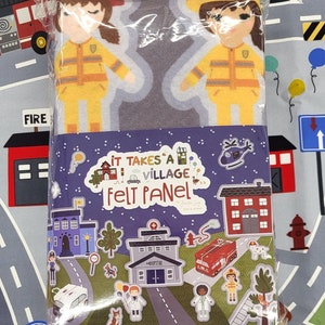 May include: A felt play set with a purple background and the text "It Takes a Village Felt Panel". The set includes a variety of buildings, vehicles, and characters, including a fire station, a hospital, a police car, and a helicopter.