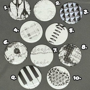 May include: A collection of ten round, black and white button pins with various designs. The designs include scissors, floral patterns, geometric shapes, musical notes, and piano keys. Some pins have text, and others feature a studded design.