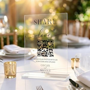 Może przedstawiać: Przezroczysty akrylowy znak ślubny z napisem "SHARE THE love" i kodem QR. Znak zawiera również imiona "OSCAR" i "NICOLE" z datą "07.18.2025". Znak jest wyświetlany na ustawieniu stołu ze złotymi świecznikami i szkłem.