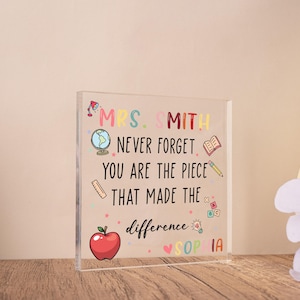 May include: A clear acrylic block with colorful text and illustrations. The text reads "MRS. SMITH NEVER FORGET YOU ARE THE PIECE THAT MADE THE difference SOPHIA." Includes a red apple, globe, and pencil.