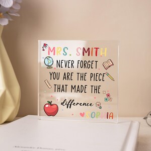 May include: A clear acrylic block with colorful text and illustrations. The text reads "MRS. SMITH NEVER FORGET YOU ARE THE PIECE THAT MADE THE difference SOPHIA". Includes a globe, apple, book, pencil, and other school-themed icons.