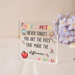 May include: A clear acrylic block with colorful text and illustrations. The text reads "MRS. SMITH NEVER FORGET YOU ARE THE PIECE THAT MADE THE difference SOPHIA." Includes a red apple, globe, and pencil. A thoughtful gift for a teacher.