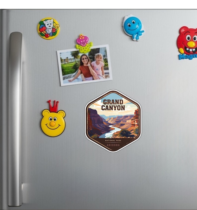 May include: A hexagonal sticker featuring a stylized illustration of the Grand Canyon in Arizona, with the text GRAND CANYON NATIONAL PARK ARIZONA. The sticker is displayed on a metallic surface alongside several colorful character magnets.