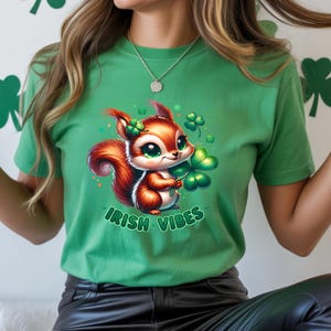 May include: Green t-shirt featuring a cartoon squirrel holding a four-leaf clover. The squirrel has brown and red fur, green eyes, and a shamrock on its head. The text "IRISH VIBES" is printed below the squirrel in green.