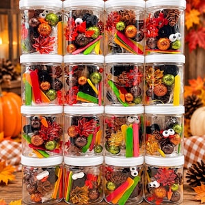 May include: A set of sixteen clear plastic jars with white lids, each filled with a craft kit containing googly eyes, small pinecones, colorful glitter balls, artificial autumn leaves, and small wooden sticks in various bright colors.