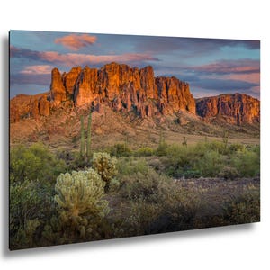 May include: A landscape photograph of a mountain range at sunset. The mountains are a reddish-orange color, and the sky is a mix of blue, pink, and orange. The foreground features desert vegetation, including cacti and shrubs.