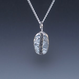 May include: A silver necklace with a detailed coffee bean pendant.