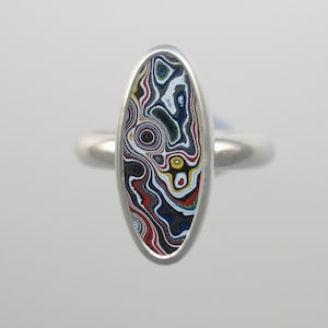 May include: A silver ring featuring an oval-shaped, multi-coloured agate stone set in the centre. The stone displays a swirling pattern of black, white, red, yellow, and blue.
