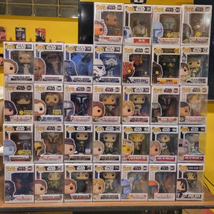 May include: A collection of thirty-five Star Wars Funko Pop vinyl figures in their original display boxes, arranged in a grid. The boxes feature various characters including Ahsoka, R2-D2, The Mandalorian, Darth Vader, and Luke Skywalker.