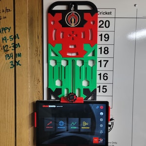 May include: A red, green, and black dartboard with a tablet displaying the Gran Board app. The dartboard is mounted on a wooden wall next to a whiteboard with numbers for scoring.
